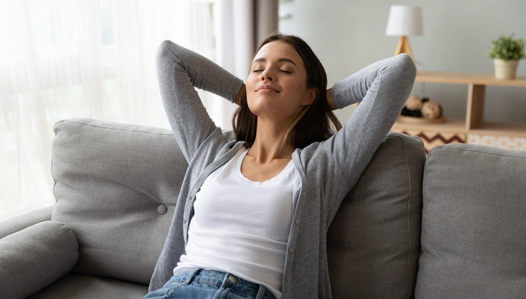 young woman relaxing back on couch being able to breath easy.