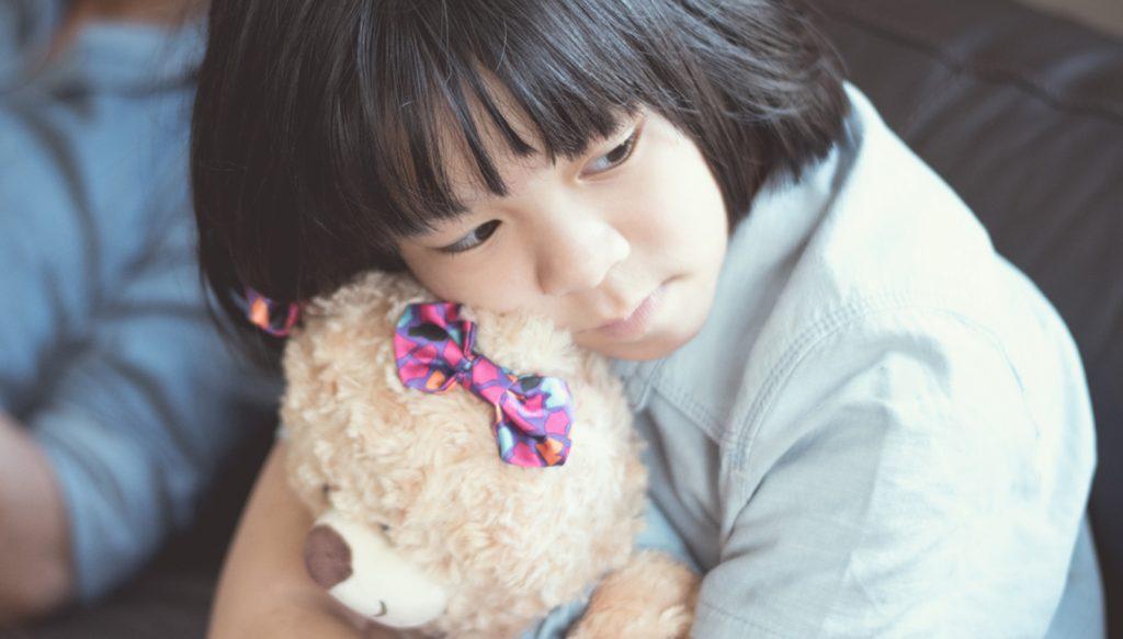 Asian little girl holding on to teddy bear.