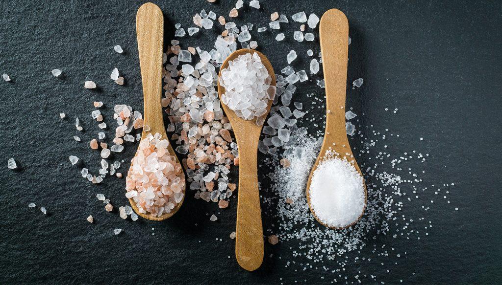 Three wooden spoons with fine salt, white salt rocks, and pink salt rocks.